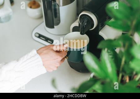 La foto della giovane donna versa il caffè dalla macchina da caffè in cucina a casa Foto Stock