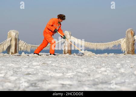 YANTAI, CINA - 27 DICEMBRE 2021 - Un operatore sanitario pulisce la neve sulla spiaggia a Yantai, provincia di Shandong, 27 dicembre 2021. Foto Stock