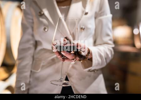 Sezione centrale di una donna caucasica sconosciuta che tiene in mano un bicchiere di vino rosso e un sigaro mentre si alza in piedi al coperto vista frontale copia spazio drink e celebratio Foto Stock