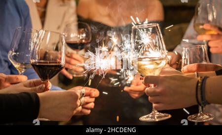 Primo piano sulle mani di un gruppo di persone che tiene bicchieri di vino e scintille durante la tostatura e la celebrazione dell'attenzione al compleanno delle scintille o del nuovo anno c Foto Stock