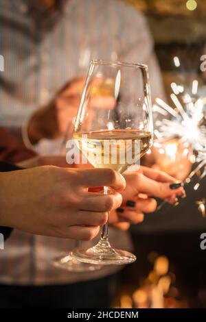 Primo piano sulle mani di un gruppo di persone che tiene bicchieri di vino e scintille durante la tostatura e la celebrazione dell'attenzione al bicchiere di vino compleanno o nuovo Foto Stock