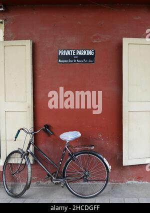 Bicicletta appoggiata su un edificio rosso murato a Bangalore, India. Foto Stock