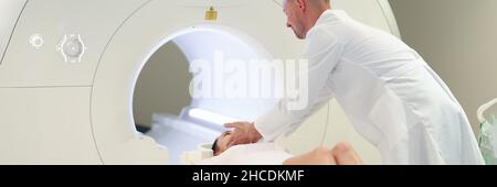 Medico che aiuta la donna a sdraiarsi in macchina mri in clinica Foto Stock