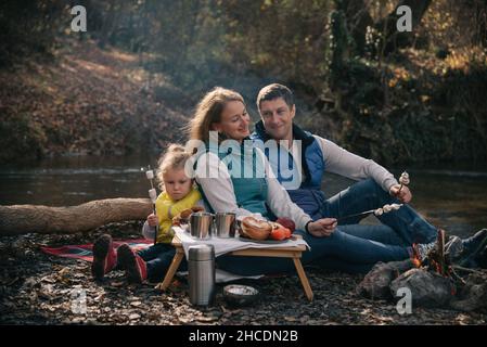 Una famiglia patisce marshmallows sui bastoni vicino al fuoco. Foto Stock