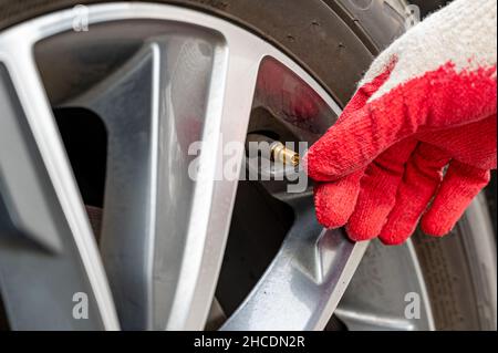 Uomo che riempie l'aria nello pneumatico. Controllo della pressione dell'aria da parte del conducente dell'auto. Foto Stock