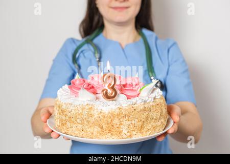 Il medico o l'infermiere tiene una torta di compleanno con il numero tre per l'anniversario dell'apertura della clinica Foto Stock