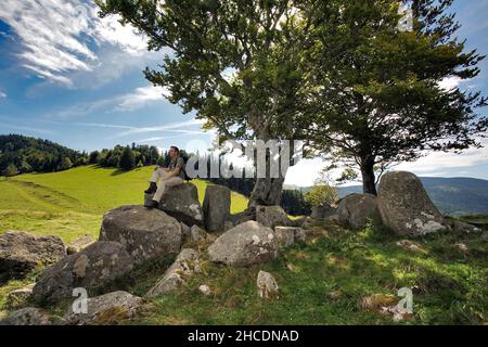 un solo uomo si siede su una roccia contro un cielo blu Foto Stock