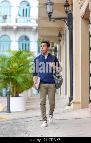 Giovane uomo latino che cammina lungo la strada con il suo computer portatile, Città di Panama, America Centrale Foto Stock