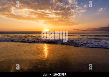 Un bellissimo e colorato tramonto sull'oceano mentre Un'onda si schianta sulla Sandy Shore Foto Stock