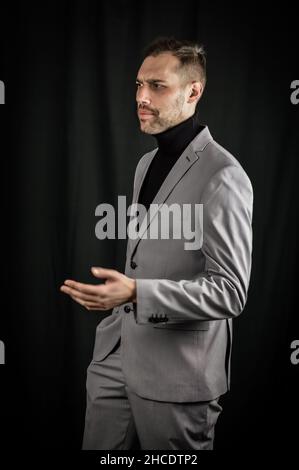 ritratto di un giovane uomo d'affari in un vestito grigio e un dolcevita nero, che preoccupava i gesticules con la mano Foto Stock
