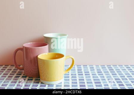 Tazzine colorate in ceramica su tavolo di piastrelle in mosaico blu. Sfondo rosa parete. Interni domestici Foto Stock