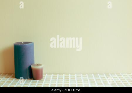 Candele blu e viola sul tavolo in ceramica mosaico. Parete di fondo beige. Interno casa Foto Stock
