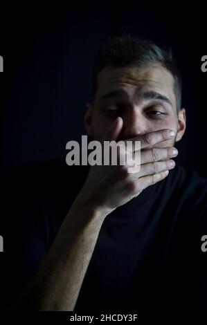ritratto di un giovane che gli copriva la bocca con la mano e che guardava imbarazzato preferendo non parlare Foto Stock