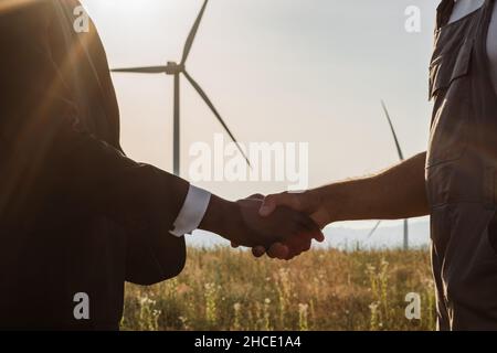 Primo piano di tecnico indiano e ispettore afroamericano che agita le mani mentre si trova in azienda con turbine eoliche. Concetto di persone, lavoro di squadra ed energia ecologica. Foto Stock