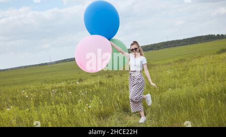 Ragazza felice con grandi palloncini multicolore in posa sul campo. Foto Stock