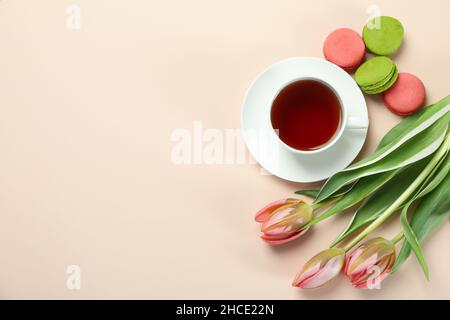 Tè, tulipani e macaroni su sfondo beige Foto Stock