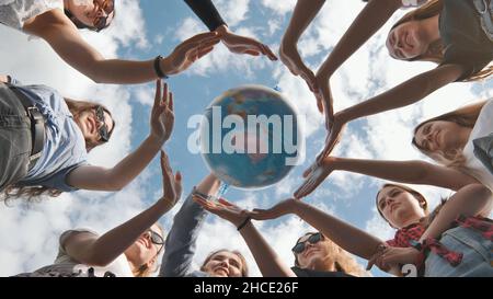 Concetto di conservazione della terra. 11 ragazze circondano il globo terrestre rotante con le loro palme. Foto Stock