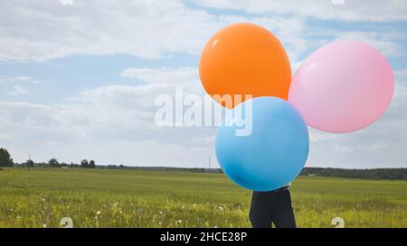 Ragazza felice con grandi palloncini multicolore in posa sul campo. Foto Stock