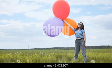 Ragazza felice con grandi palloncini multicolore in posa sul campo. Foto Stock