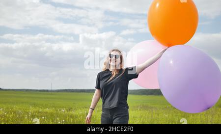 Ragazza felice con grandi palloncini multicolore in posa sul campo. Foto Stock