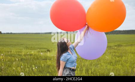 Ragazza felice con grandi palloncini multicolore in posa sul campo. Foto Stock