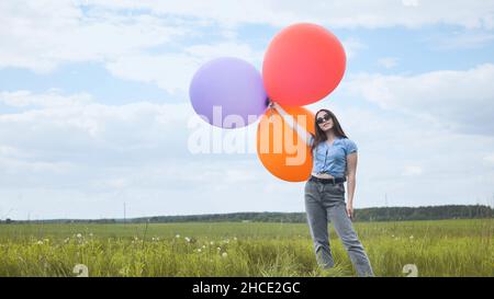 Ragazza felice con grandi palloncini multicolore in posa sul campo. Foto Stock