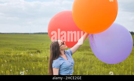 Ragazza felice con grandi palloncini multicolore in posa sul campo. Foto Stock