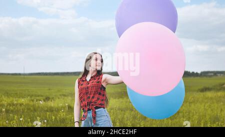 Ragazza felice con grandi palloncini multicolore in posa sul campo. Foto Stock