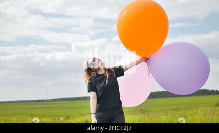 Ragazza felice con grandi palloncini multicolore in posa sul campo. Foto Stock