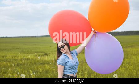 Ragazza felice con grandi palloncini multicolore in posa sul campo. Foto Stock