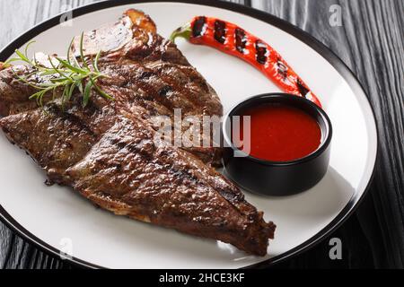 Succosa bistecca con osso a T, grigliata con erbe, salsa di pomodoro e peperoncino in un piatto su un tavolo di legno. Orizzontale Foto Stock