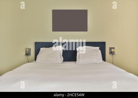 Letto confortevole con cuscini in camera spaziosa con pareti colorate in appartamento moderno Foto Stock