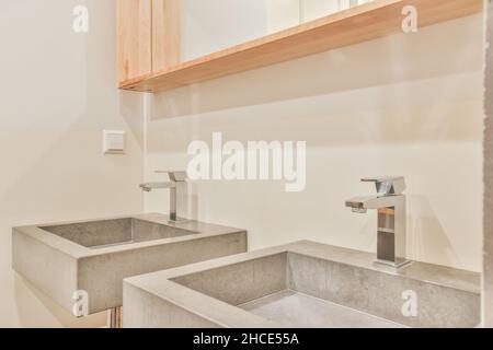 Lavandini in pietra scura e specchio in un bagno moderno illuminato con dettagli in legno Foto Stock