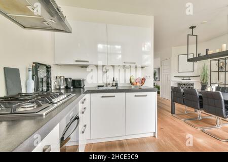 Interno di cucina contemporanea con zona pranzo arredato con tavolo circondato da sedie di pelle e lampadario moderno appeso Foto Stock