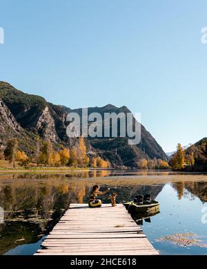 Vista laterale di viaggiatore femminile irriconoscibile seduto sulla passerella di legname del molo vicino alle acque calme di Torrassa Reservoir e giocando con il cane in soleggiato da Foto Stock