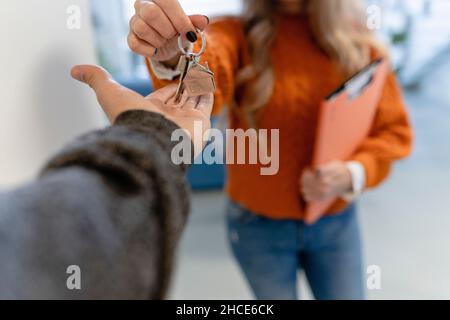 Ritagliare irriconoscibile realtor femminile con documenti che danno le chiavi da appartamento a uomo senza volto, mentre in piedi in stanza su sfondo sfocato Foto Stock