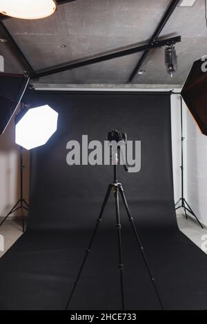 Interno di moderno studio fotografico con octabossi e fotocamera professionale su treppiede su sfondo nero Foto Stock