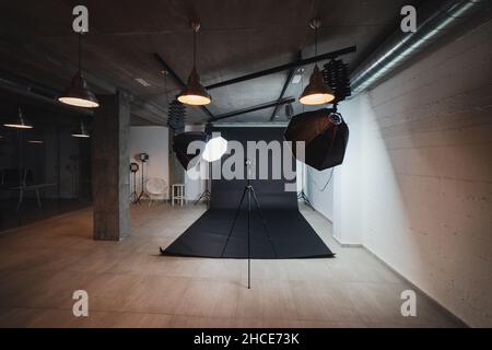 Interno di moderno studio fotografico con octabossi e fotocamera professionale su treppiede su sfondo nero Foto Stock