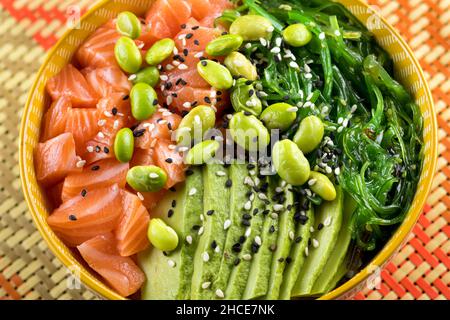 Da sopra di appetitoso e sano poke ciotola con salmone tritato e verdure saporite posto sul tavolo Foto Stock