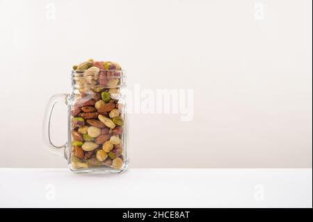 Vaso di vetro riempito con una varietà di nutrizione e snack sani e noci su uno sfondo bianco Foto Stock