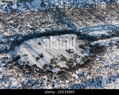 Sterrato, strada sterrata. È una mattina d'inverno. Il terreno è coperto da uno strato di neve, l'acqua nella pozzanghera è ghiacciata. Foto Stock