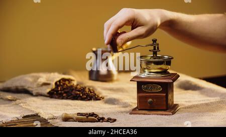 vista ritagliata dei chicchi di caffè macinati dall'uomo vicino alla caffettiera sfocata, immagine stock Foto Stock