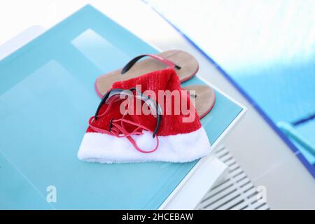 Cappello di Babbo Natale, ciabatte da bagno sul lettino solare Foto Stock
