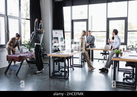 donna che mostra il gesto di vincere giocando a calcio da tavolo con un collega afroamericano in ufficio Foto Stock