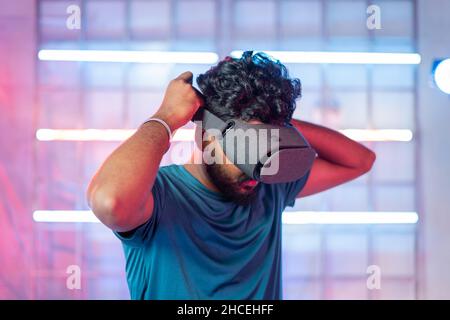 Videogamer professionista che indossa la realtà virtuale con il dispositivo mobile all'interno del visore prima di giocare: Il concetto di tecnologia di gioco moderna viene mostrato su sfondo chiaro al neon Foto Stock