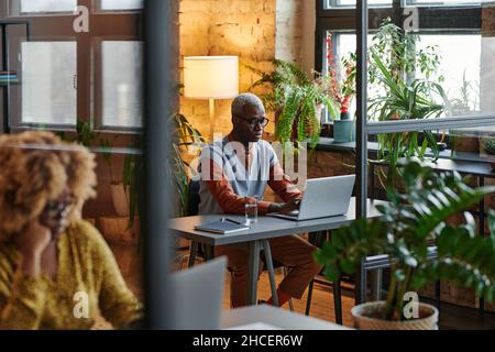 Un uomo d'affari africano che si concentra sul suo lavoro online in ufficio, seduto sul suo posto di lavoro e digitando sul portatile Foto Stock