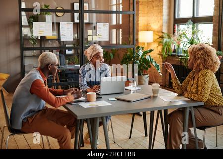 Gruppo di uomini d'affari seduti al tavolo con un computer portatile e che pianificano di lavorare insieme durante una riunione d'affari in ufficio Foto Stock