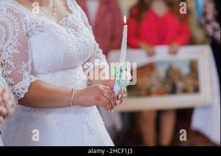 La sposa e lo sposo tengono candele lucenti durante la cerimonia nella chiesa. Mani di sposi novelli con candele nella chiesa. Chiesa religiosa dettagli Foto Stock