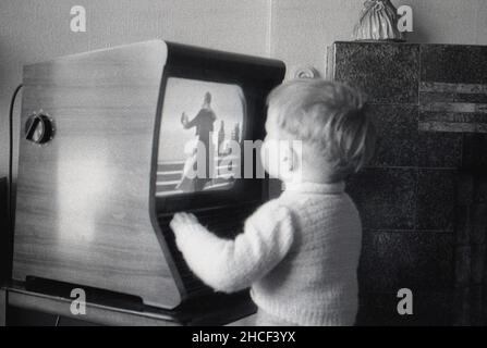 1950s, storico, all'interno di una sala d'ingresso, un ragazzino che si alza vicino ad un piccolo televisore dell'epoca che guarda un programma, Inghilterra, Regno Unito. Foto Stock