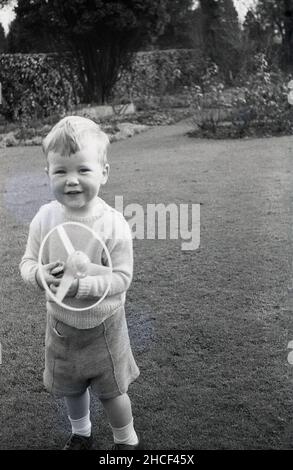 Fine del 1950s, storico, fuori in un giardino, un ragazzino con il suo nuovo giocattolo, un top portatile rotante, Inghilterra, Regno Unito. I giocattoli di estrazione erano un giocattolo popolare in questo decennio ed è venuto in una varietà di forme. Foto Stock